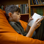 Boy sitting in orange beanbag chair reading a book.