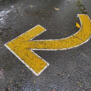 a yellow arrow pointing left on an asphalt street
