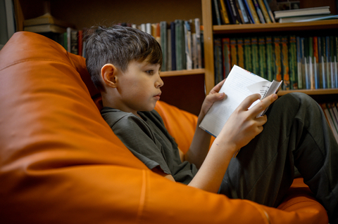 Boy sitting in orange beanbag chair reading a book.