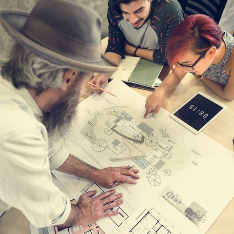 Three people reviewing architectural plans on a table.