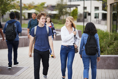 Students walking together on campus with backpacks and casual outfits.