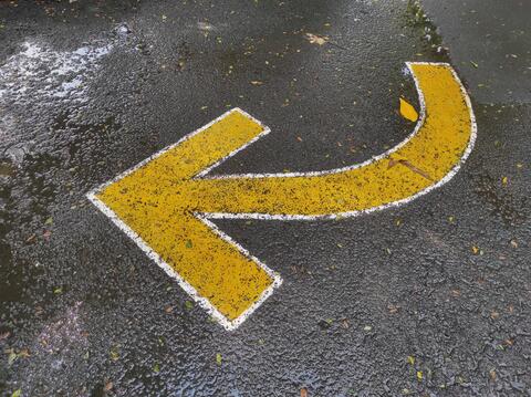 a yellow arrow pointing left on an asphalt street