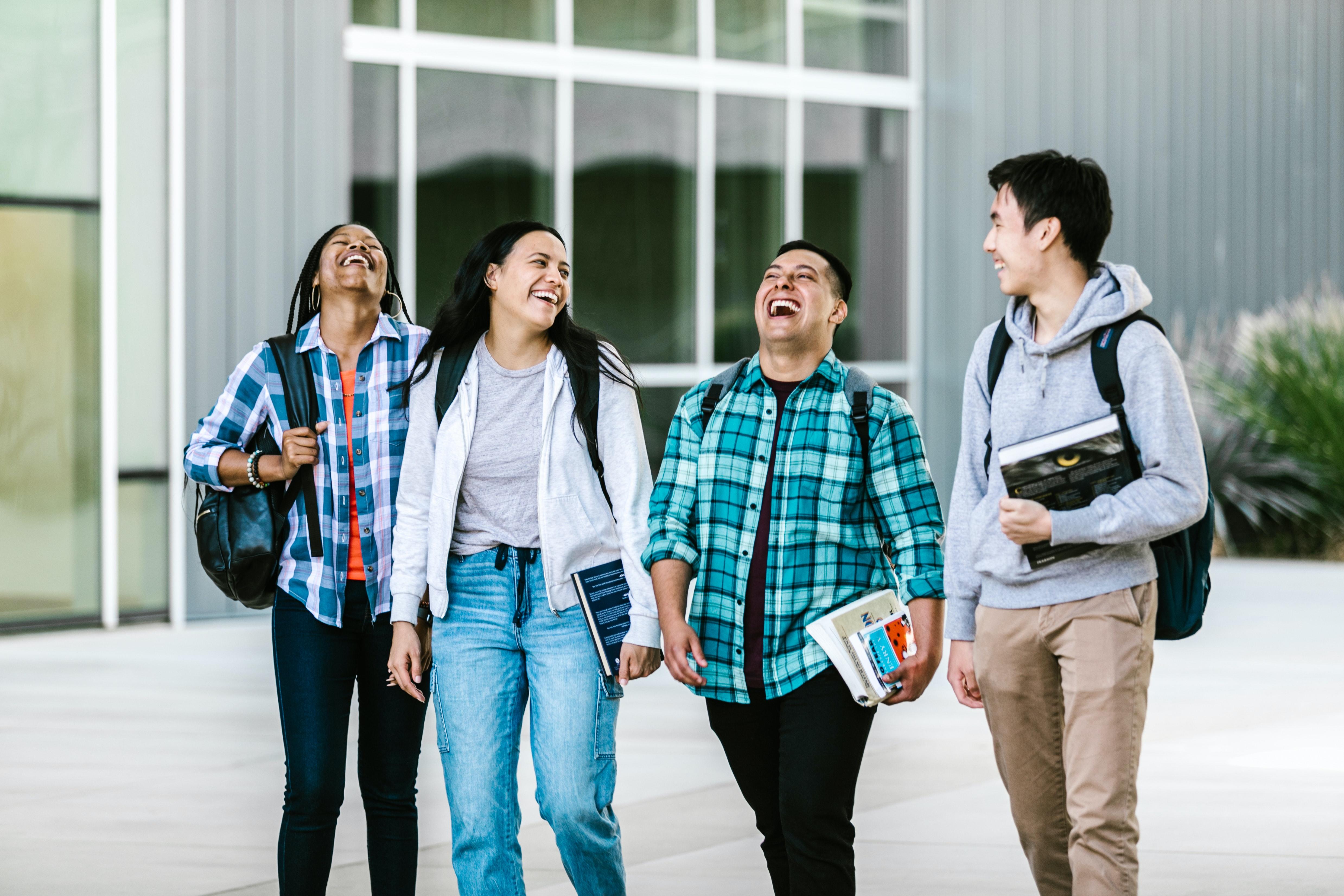 A group of students laughing while walking across a college campus.